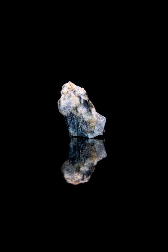 A raw mineral with a reflection on a shiny black surface, showcasing its natural texture.