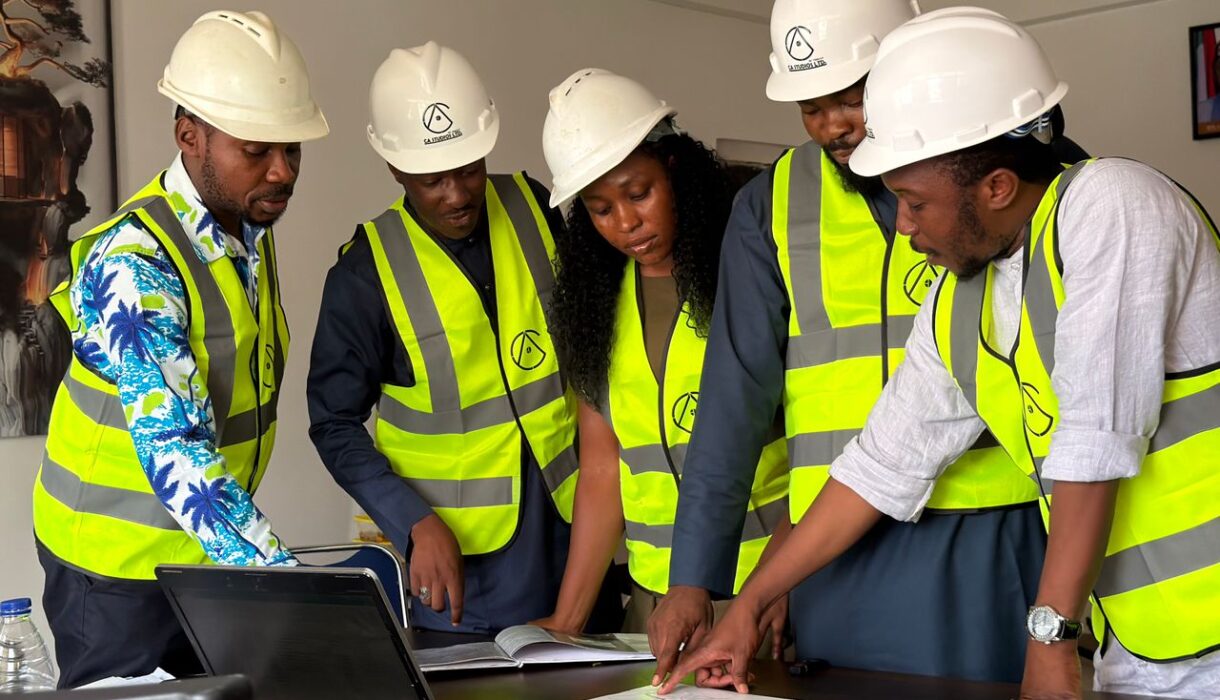 Group of engineers in safety gear reviewing blueprints indoors.